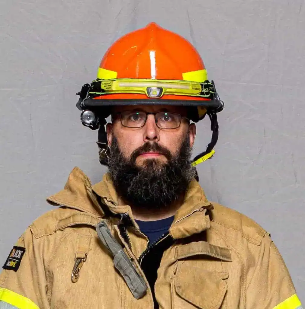 Peter Myers, rookie with the Bahama Volunteer Fire Department, in full turnout gear and an orange helmet with mounted lights, facing forward in a formal portrait.