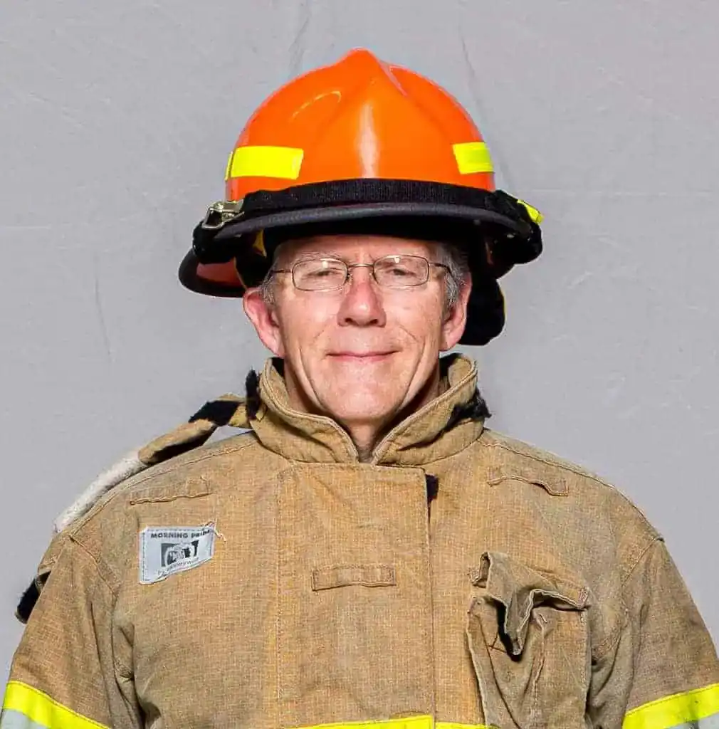Christopher Brown, rookie with the Bahama Volunteer Fire Department, wearing full turnout gear and an orange helmet, smiling in a professional portrait.