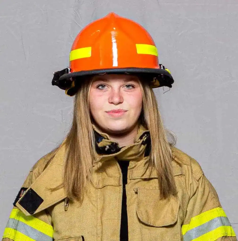 Adriana Cannady, rookie with the Bahama Volunteer Fire Department, wearing full turnout gear and an orange helmet, facing forward in a professional portrait.