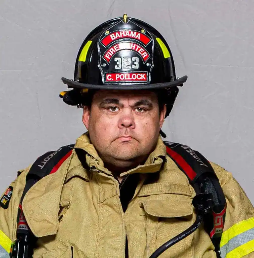 Charlie Pollock, Captain of the Bahama Volunteer Fire Department, in full turnout gear and a black helmet labeled “Firefighter 323,” posing for a formal portrait.