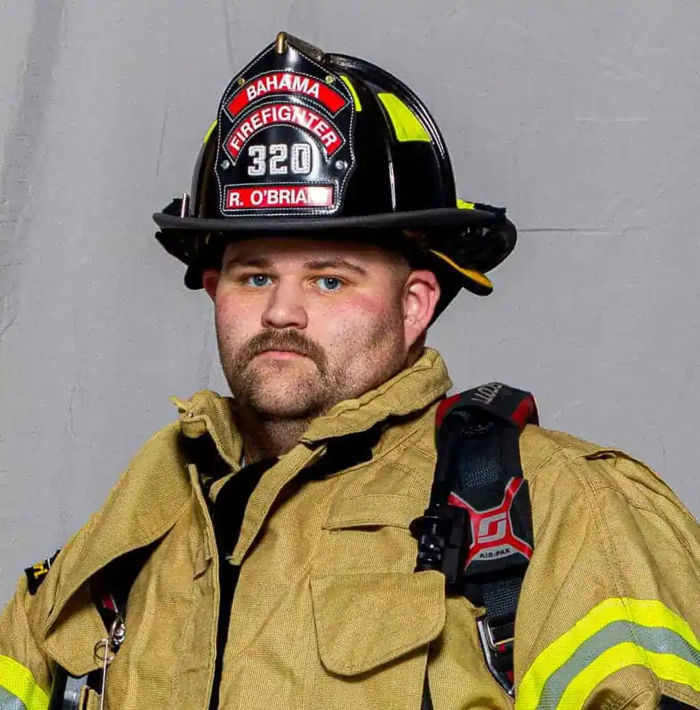David Weatherspoon, Assistant Chief of the Bahama Volunteer Fire Department, in full turnout gear and a white helmet with a gold "Assistant Chief" shield, posing for a formal portrait.