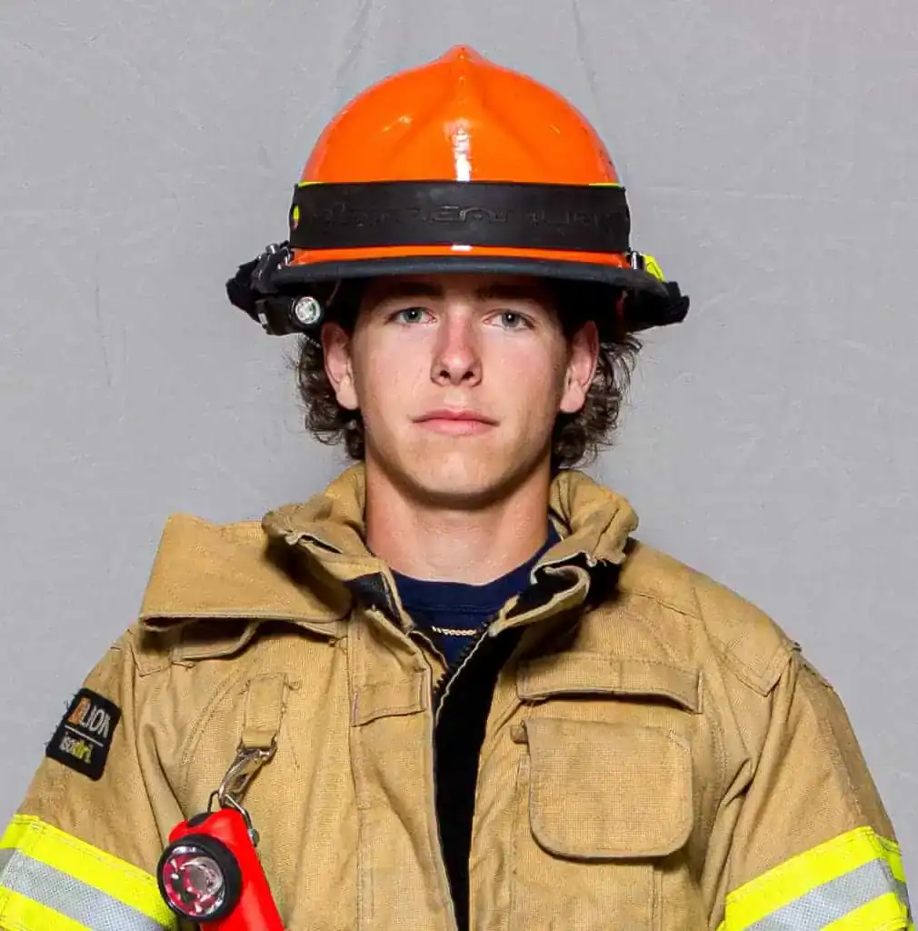 Elijah Horton, rookie with the Bahama Volunteer Fire Department, wearing full turnout gear and an orange helmet, facing forward in a professional portrait.