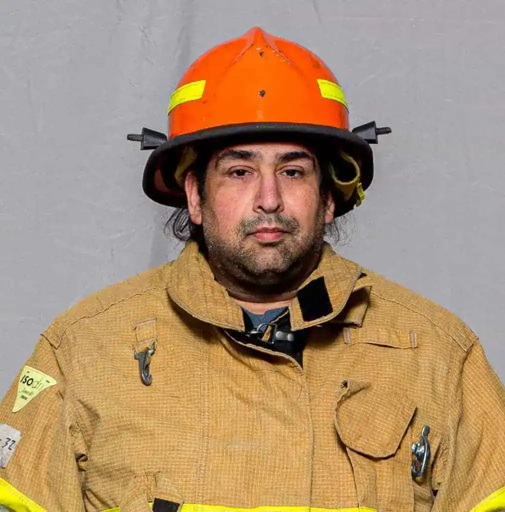 Lawrence Praino, EMT with the Bahama Volunteer Fire Department, in full turnout gear and an orange helmet, facing forward in a professional portrait.