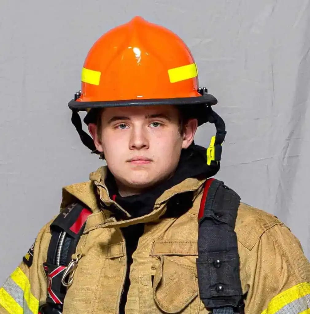 John Nieman, rookie with the Bahama Volunteer Fire Department, in full turnout gear and an orange helmet, facing forward in a professional portrait.