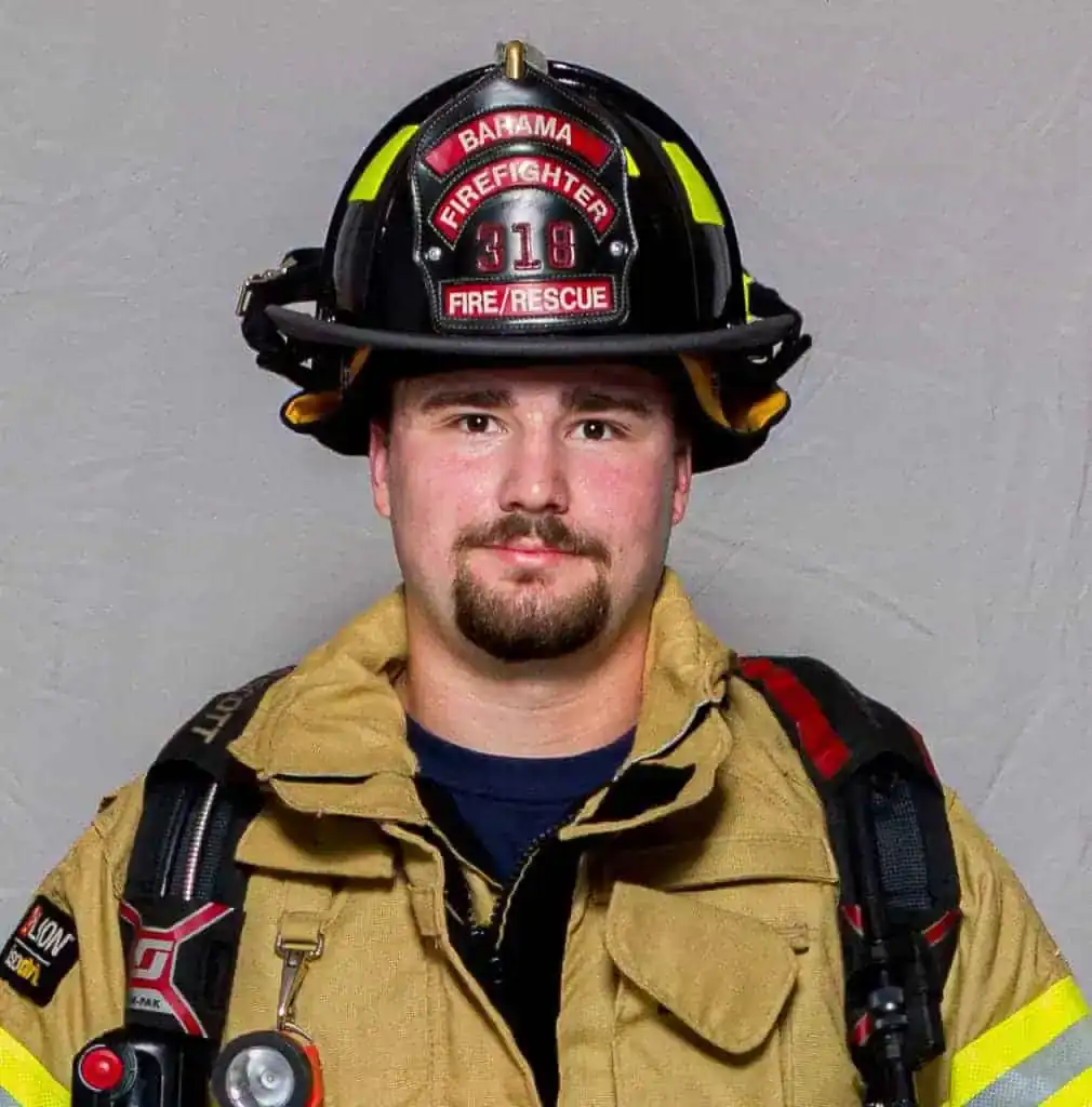 Ethan Minton, firefighter with the Bahama Volunteer Fire Department, wearing full turnout gear and a black helmet labeled “Firefighter 318,” facing forward in a formal portrait.