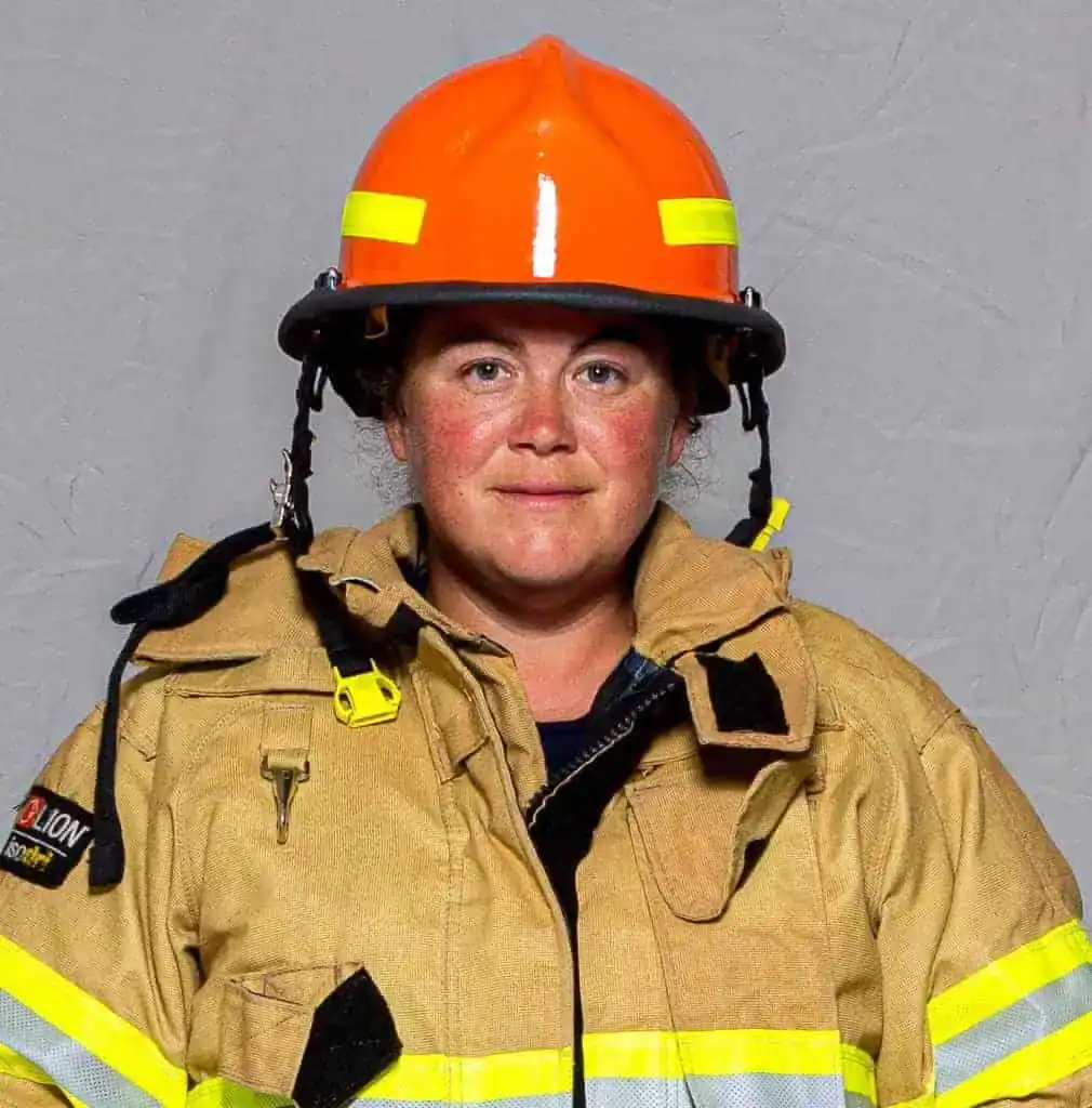 Audrey Sandifer, EMT with the Bahama Volunteer Fire Department, wearing full turnout gear and an orange helmet, facing forward in a formal portrait.